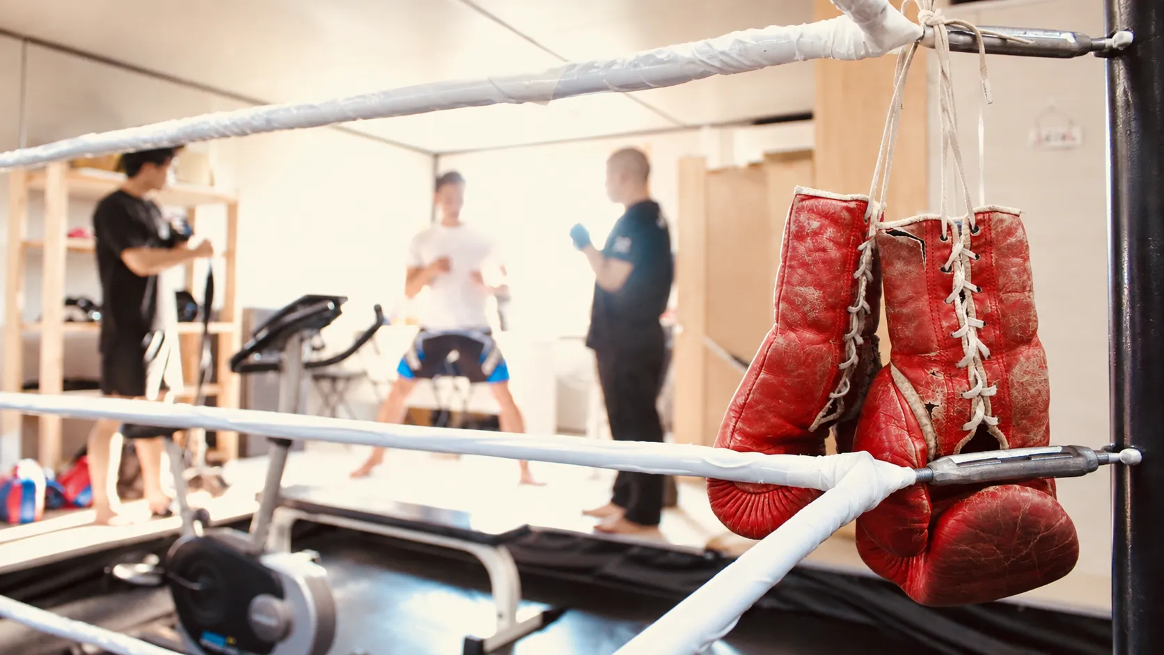 伊万里のキックボクシング＆フィットネス OCEAN GYM。リングに掛けられた赤いグローブの奥で会員がトレーニングしている様子
